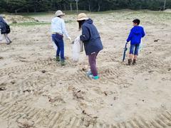 手にゴミ袋を持って、海岸のゴミ集めを行っている参加者の方々を後方から写した写真