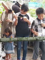 竹で作った流し台でそうめん流しを楽しんでいる男の子と女の子の写真