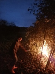 周りは暗い夜空で、竹を組み立てて作ったやぐらの側で、男性が火を入れて赤々と燃え始めている写真