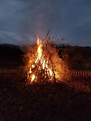 竹を組み合わせて作ったやぐらが、暗い夜空に煙を出し、赤々と燃えているどんど焼きの様子の写真