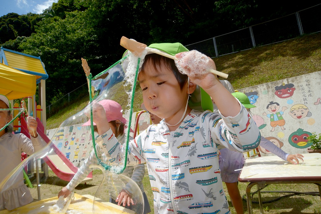 男児が、ひものわっかにふーっと息を吹きかけ、シャボン玉を作っている様子