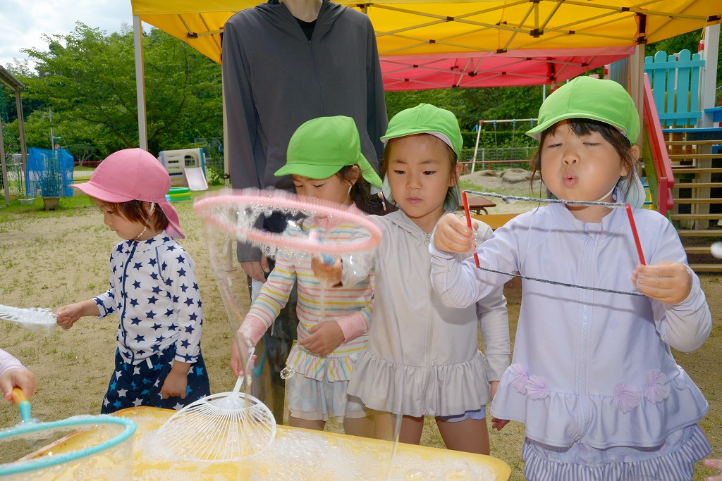園児たちが、ひもやプラスチックの輪っかやのにシャボン玉液をつけ「ふー」と吹いている様子
