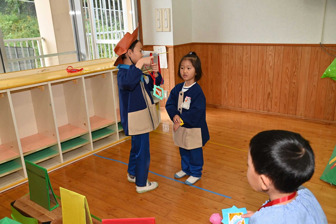 年長男児が、年中女児の首にに手作りペンダントをかけてあげている様子