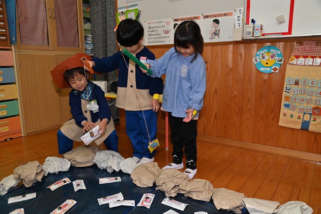 園児2名が釣りをして、そのうち1名の竿に魚がくっつき、年長児がはずしてあげている様子