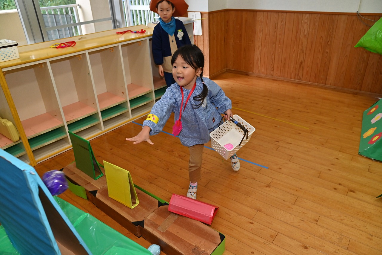 年少女児が恐竜的当てに向かって、笑顔でボールを投げている様子