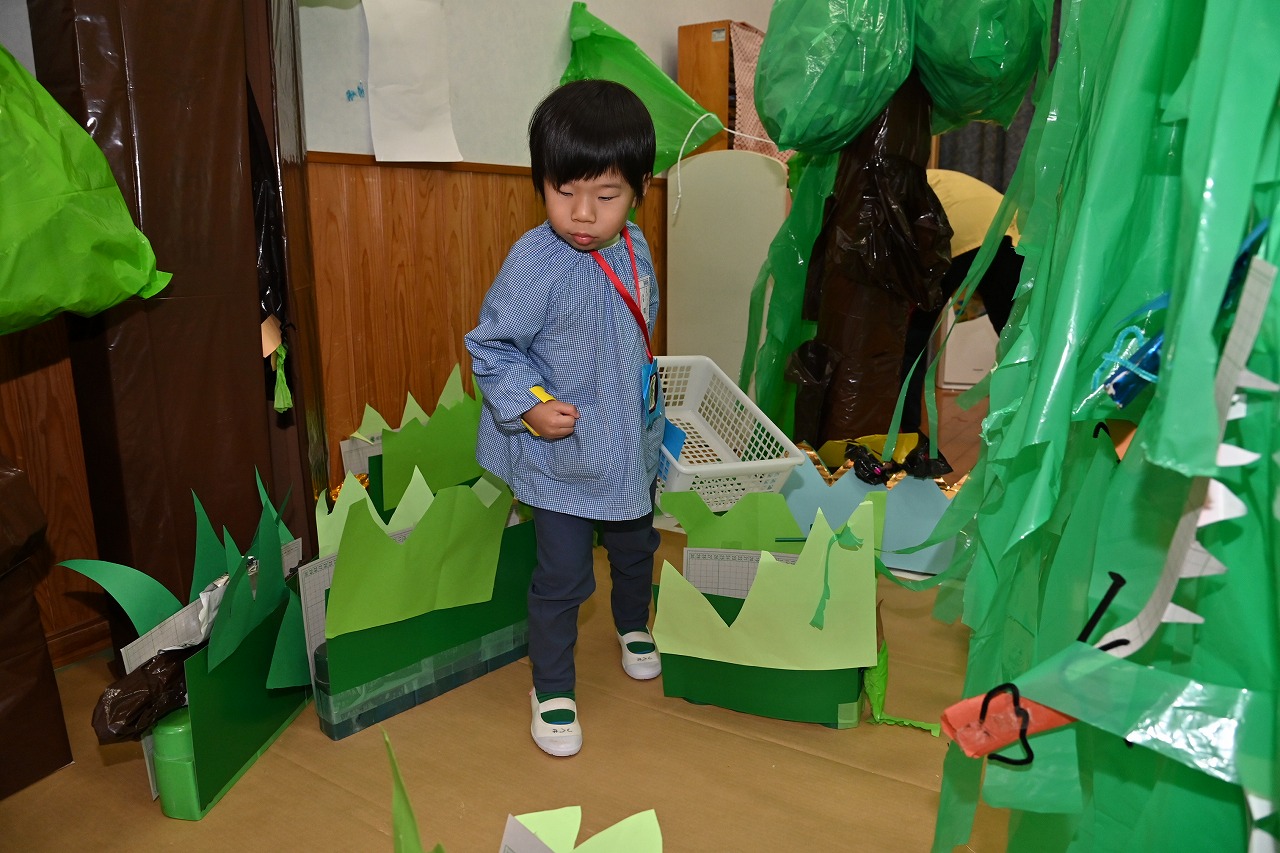 ダンボールやカラービニール袋、画用紙で作られた森の中に、手作りの虫が隠されていて、男児1名がそれを探している様子