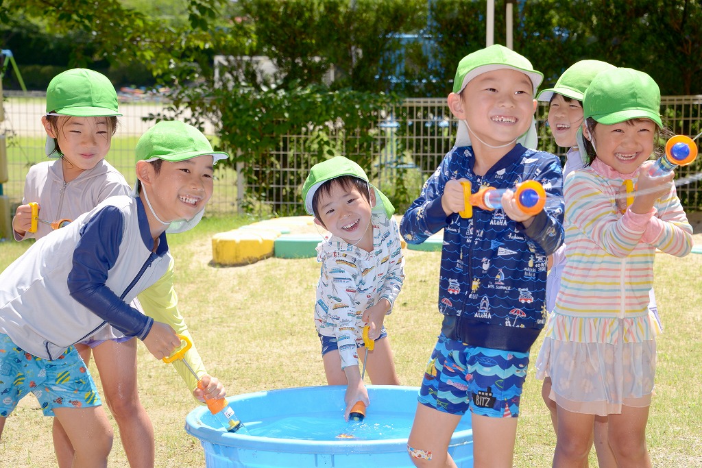 年長園児が水鉄砲に水を入れ、笑顔で水を飛ばしている様子