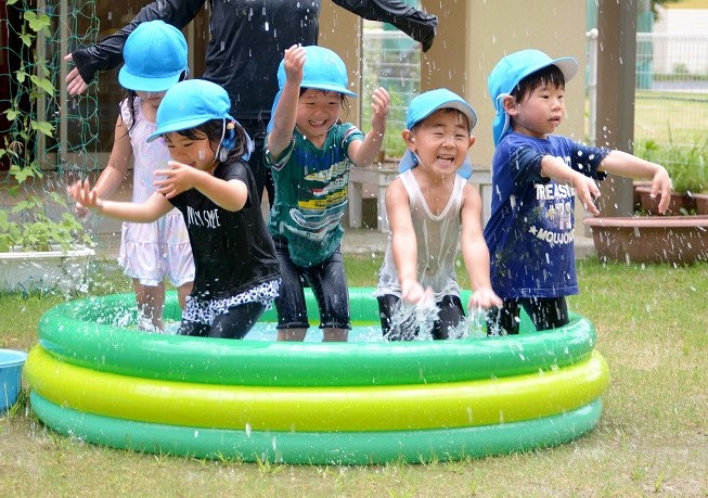園児5名がビニールプールに入って、水を書開け合っている様子