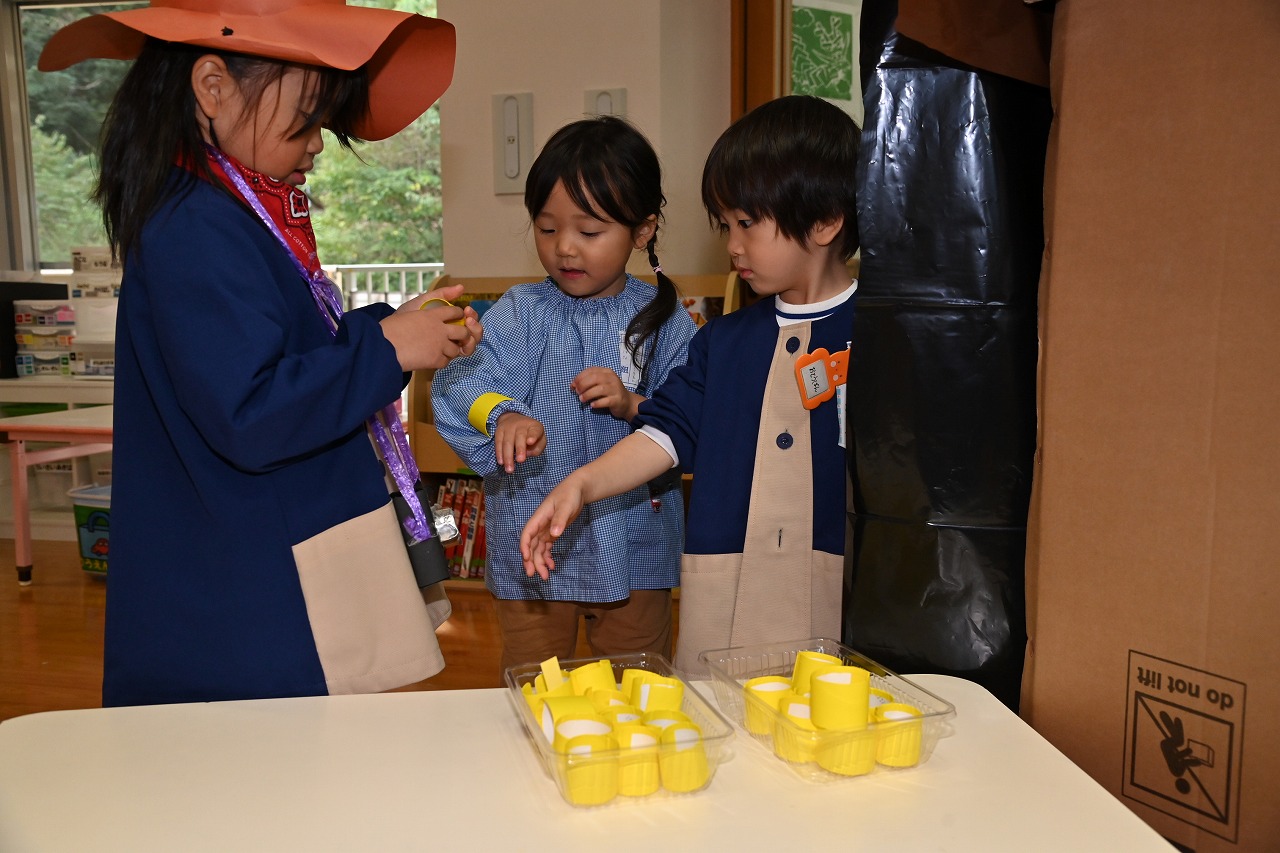 年長女児が、洞窟トンネルの入り口で、年少年中児に腕輪をつけてあげている様子