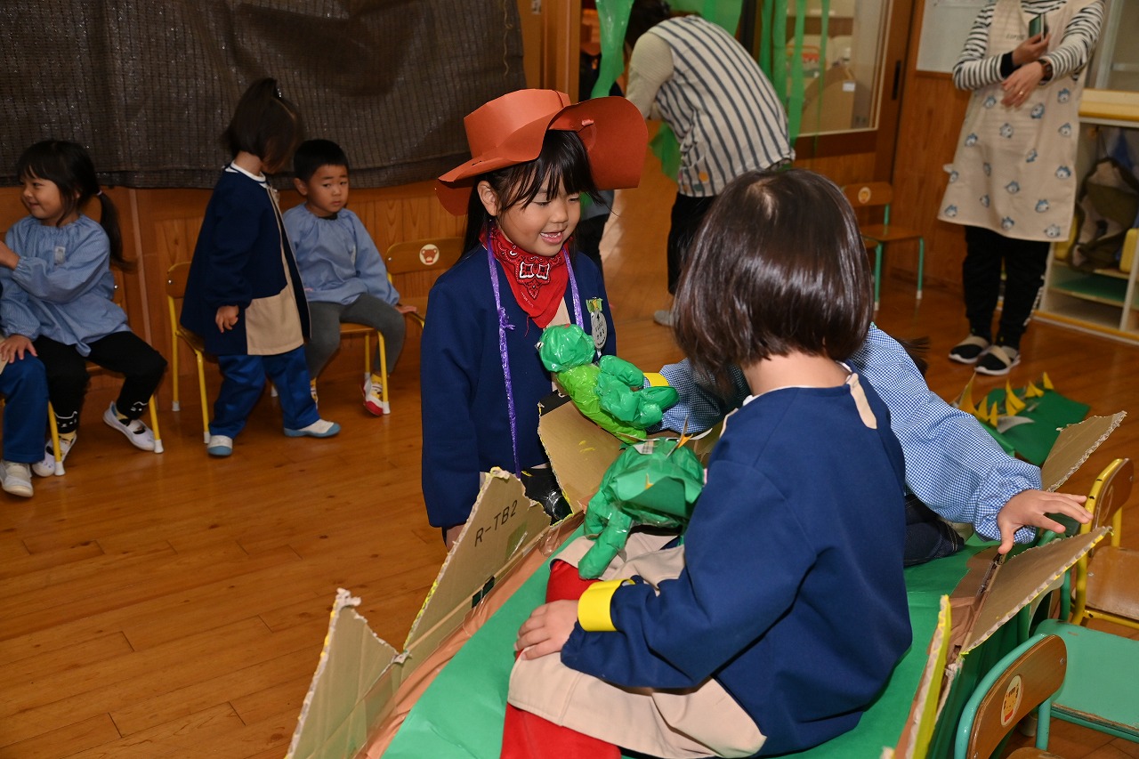 年長女児が、ダンボールで作られたステゴザウルスの背中に、年少年中児を載せている様子