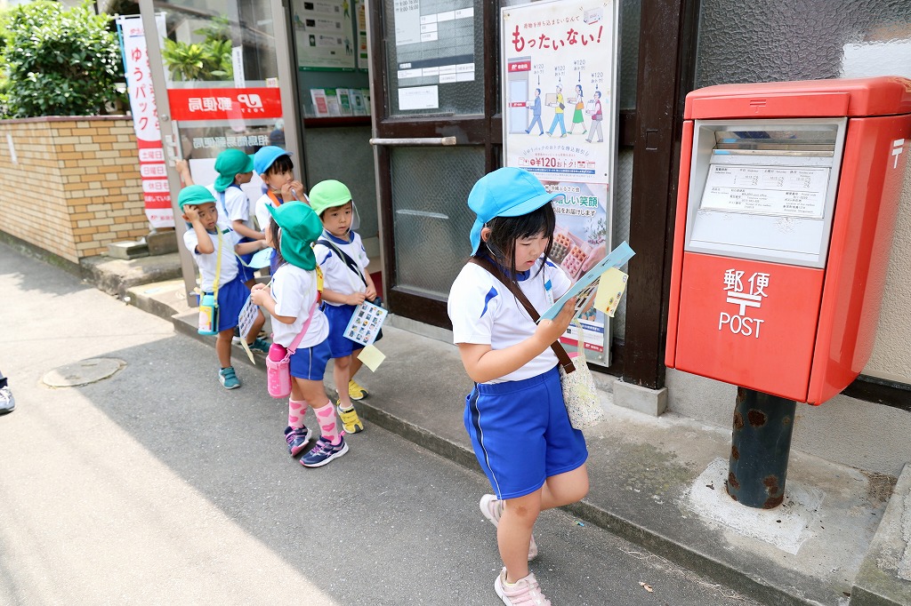 園児が探検カードを見ながら郵便局の前を歩いている様子