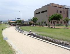 奥に建物があり中央に遊歩道、歩道の右側に小さな川が流れている沖田中央公園の写真