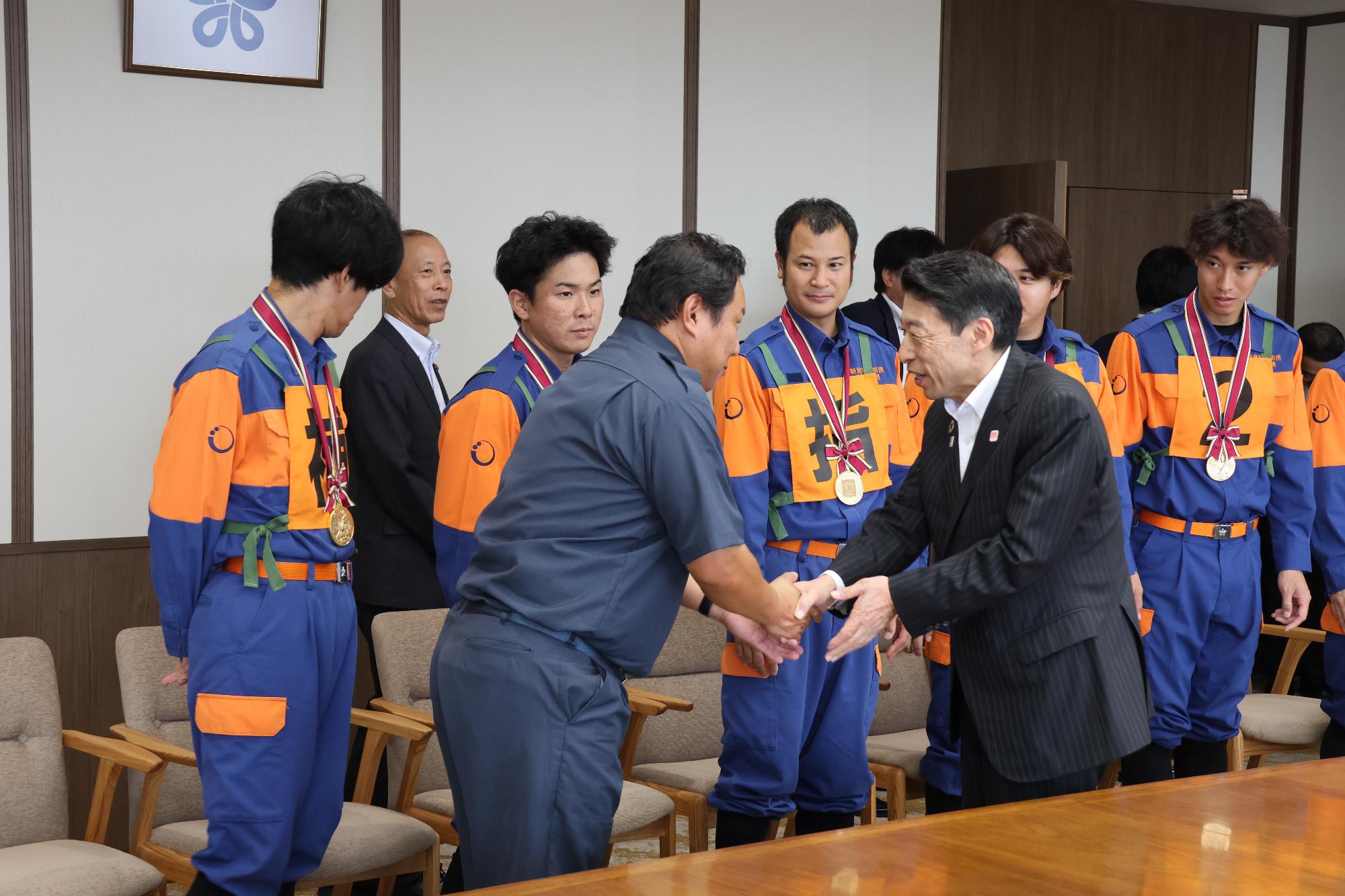 福岡県知事と握手する消防団長と団員の様子