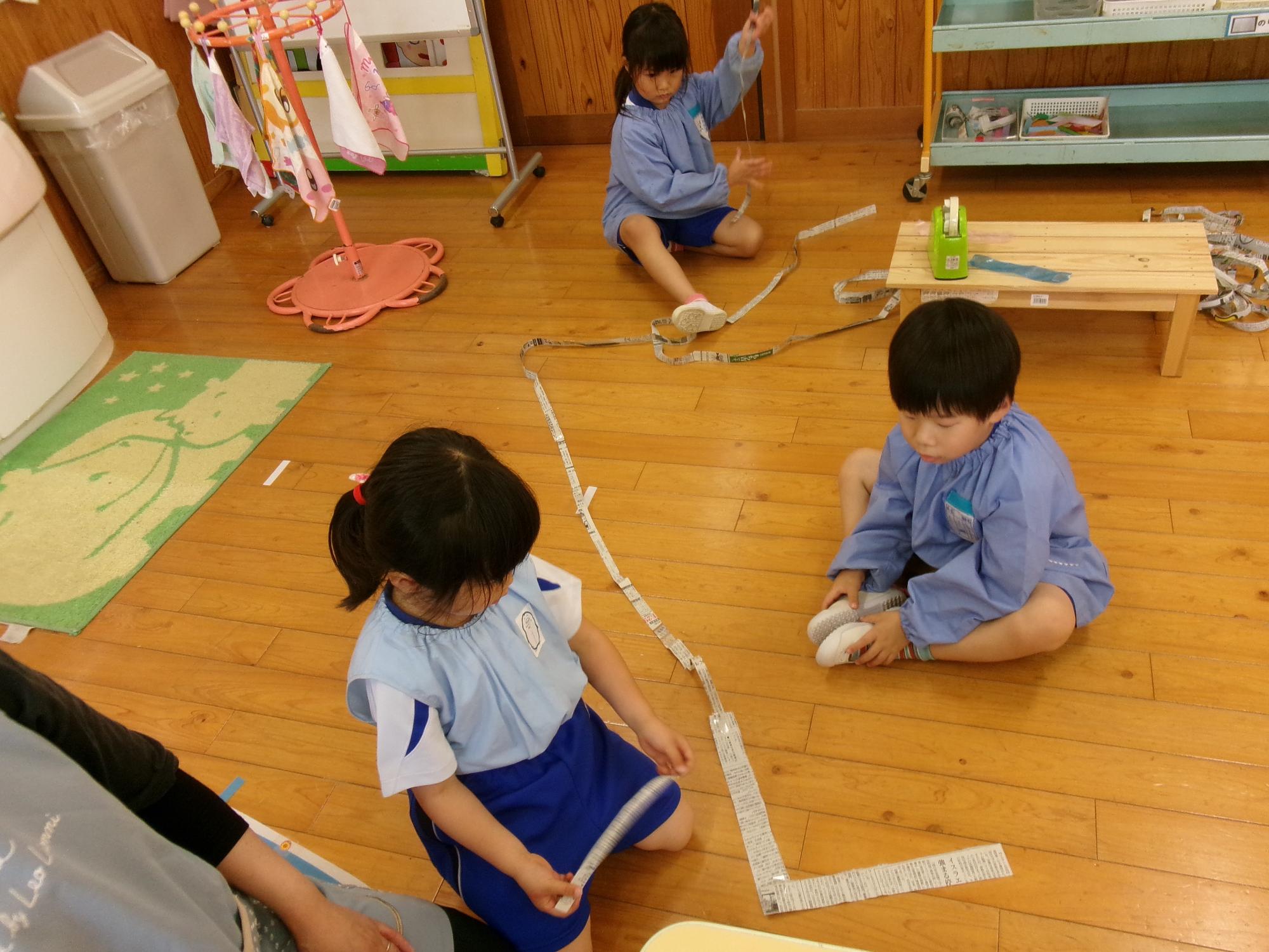 細長く切った新聞紙をつなげて遊ぶ年中児