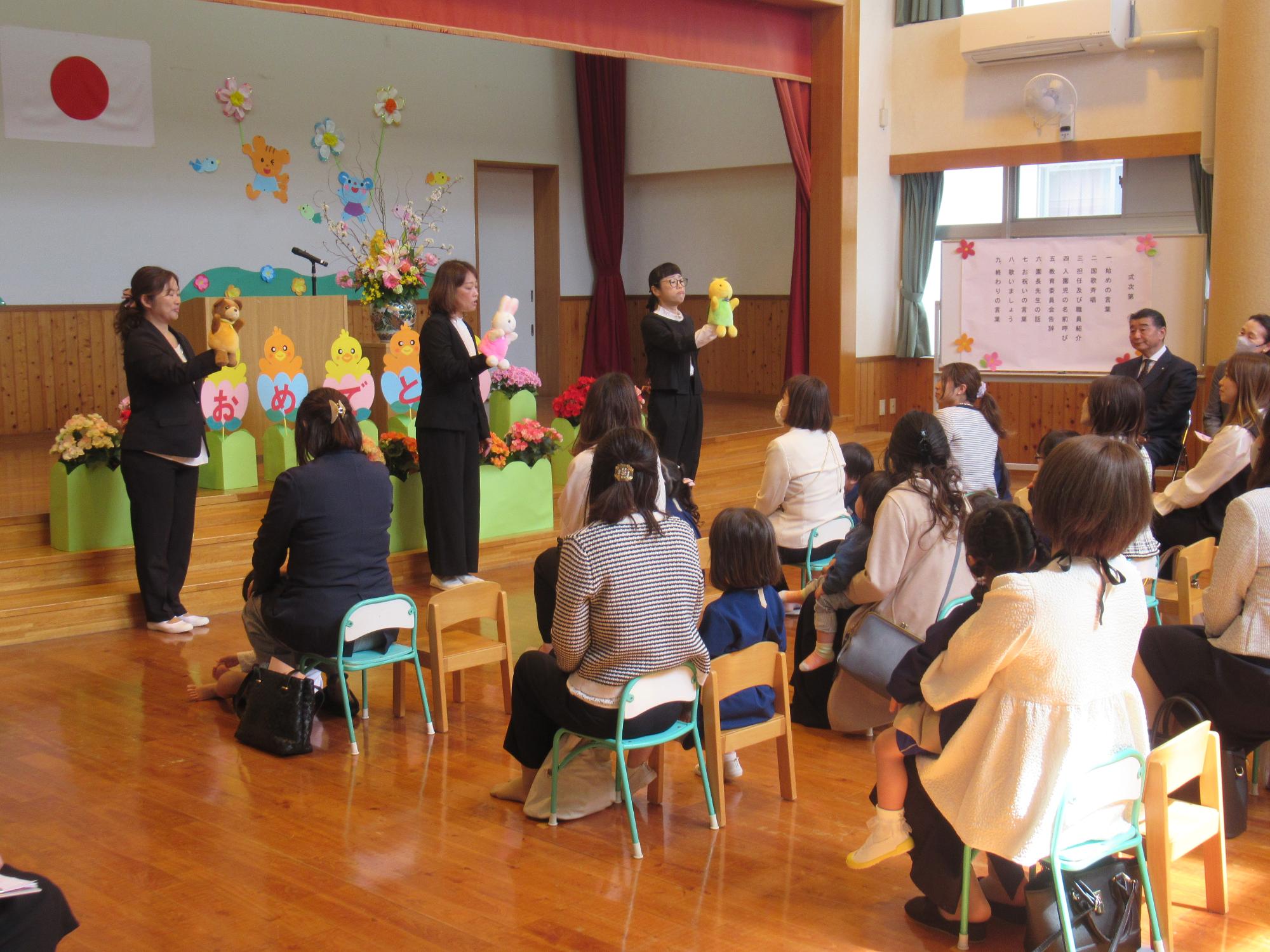 入園式で先生たちが演じる人形劇を見て、明日から園に来ることを楽しみにしている入園児とその保護者