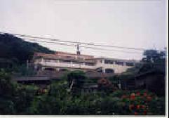 周りが山に囲まれた場所にあり、白壁に茶色の屋根の新宮中学校相島分校を遠くから撮った外観写真