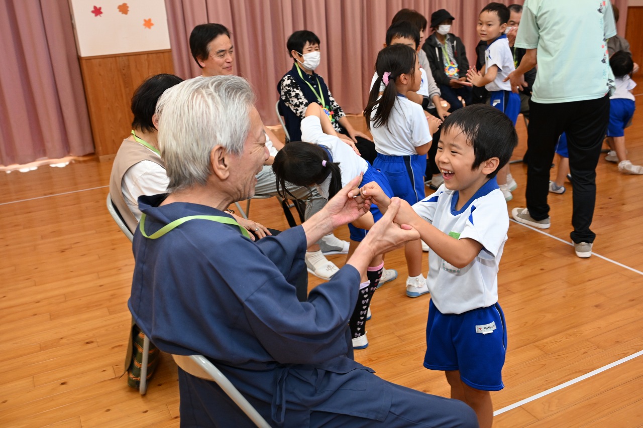 男児とおじいちゃんが手をつないで笑顔で見つめ合っている様子