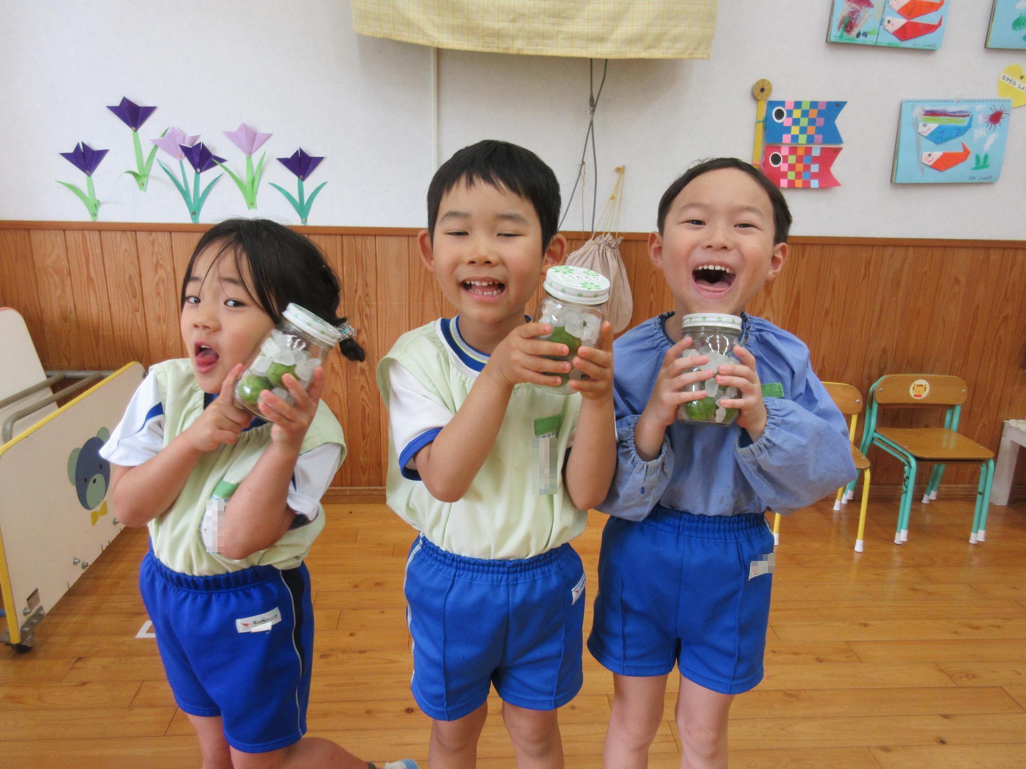 園児3名が梅ジュースの瓶を持って、笑顔でポーズをとっている様子