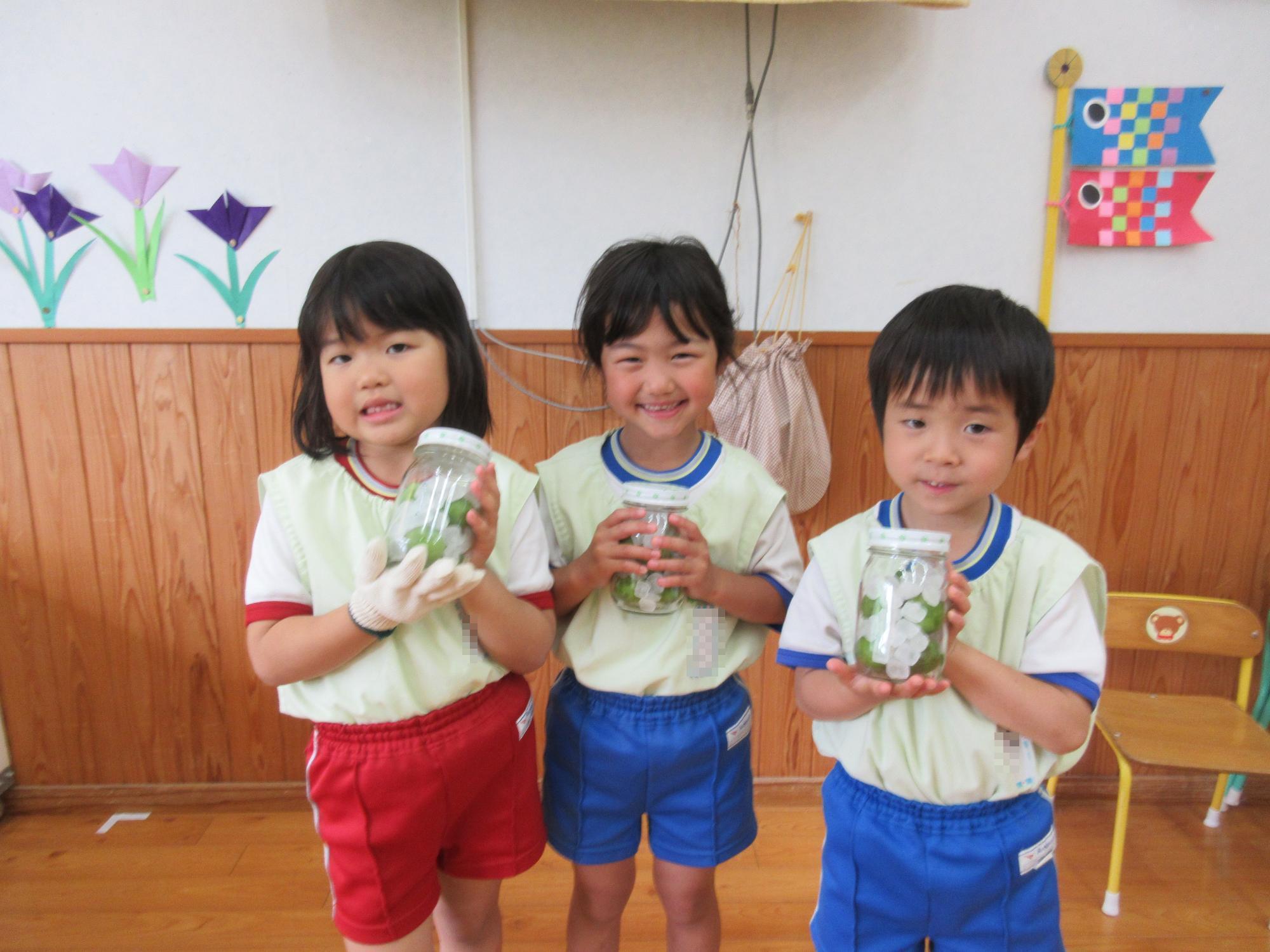 園児3名が梅ジュースの便瓶を持って、笑顔でポーズをとっている様子