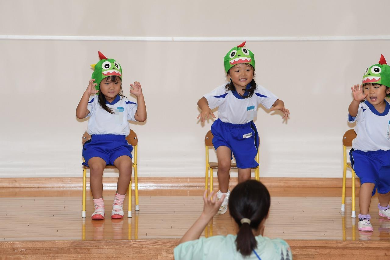 年少女児がステージで、椅子に座って手遊び歌を発表している様子