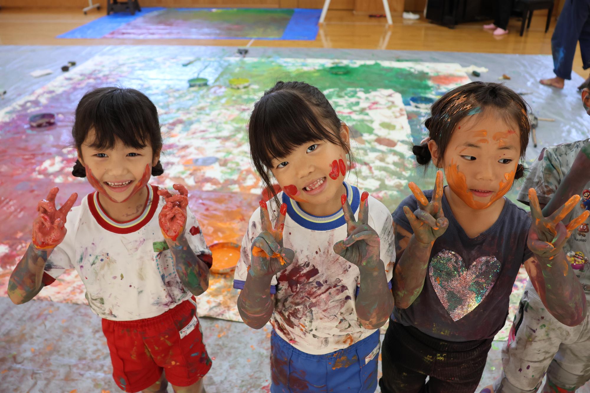 顔に絵具をつけた女児3人が笑顔でポーズをとっている様子