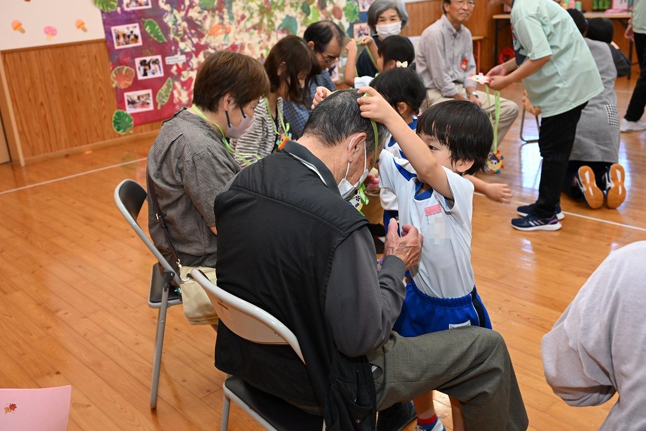 園児がおじいちゃんの首にペンダントをかけてあげている様子