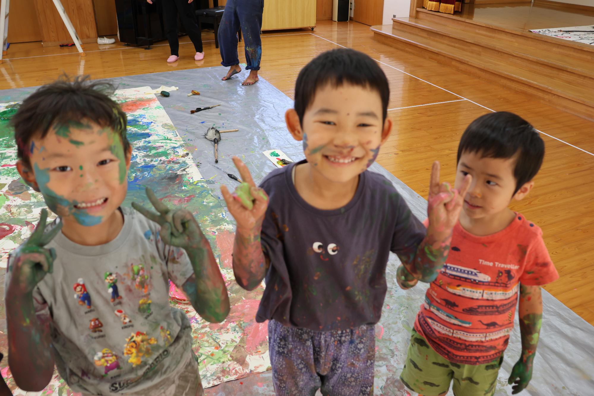 顔に絵具をつけた男児3名が笑顔でポーズをとっている様子
