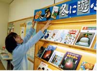 本が並べられた特設コーナーで、本棚の上に手作りのポスターを貼っている女性の写真