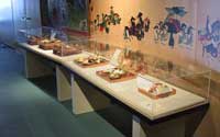 絵画の前に置かれた展示ケースの中に6つの饗応食のレプリカが展示されている写真