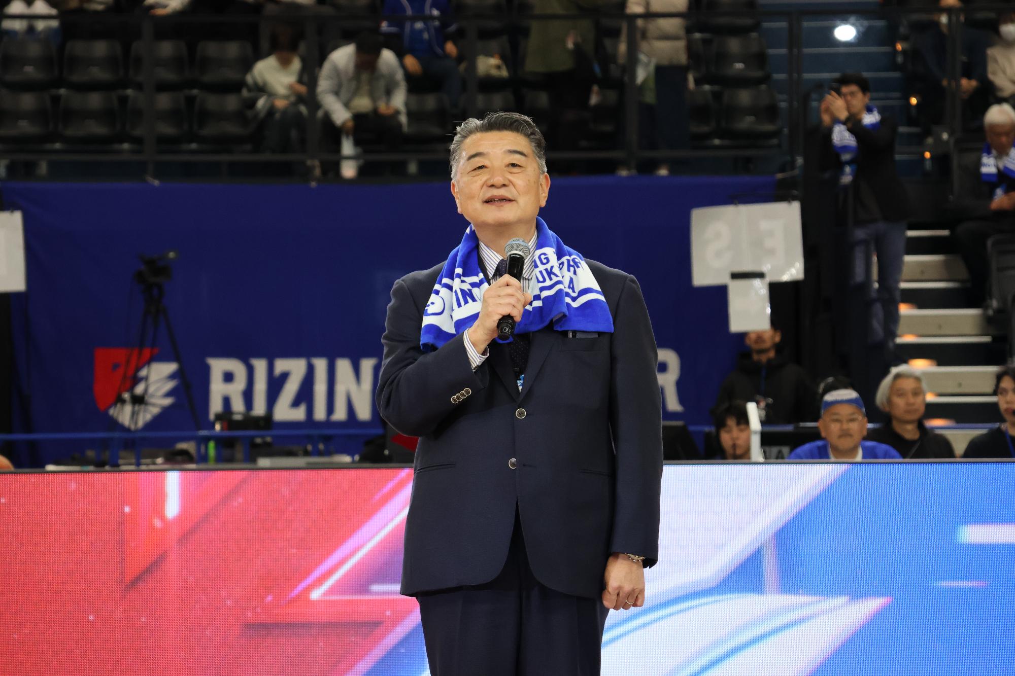 ライジングのマスコットキャラジン君とチアのアールサンズの間であいさつを行なう町長