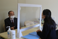 町長と女性が、パーテーション越しに向かい合って座り、話をしている写真