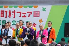 カラフルな法被を着た町長や関係者が、舞台に立ち袋を持っている写真